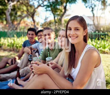 L'unico modo per godersi l'estate. Ritratto corto di una giovane donna attraente godendo un paio di bevande con gli amici fuori nel sole estivo. Foto Stock