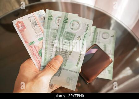 Banconote in contanti Dirham in mano con il portafoglio. Istruzione finanziaria e tasso di cambio AED Foto Stock