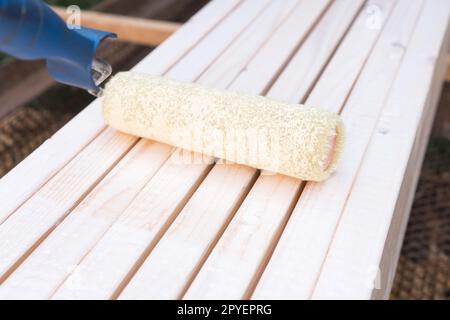 Vista laterale dell'applicatore a rulli per pittura morbida bianca per pareti e pavimenti colorati, banco in legno a spazzola per esterni. Cantiere Foto Stock