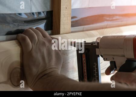 Mani per costruttori corti che reggono pistola chiodatrice pneumatica, graffatrice per pannelli di legno. Rigatura, impostazione dei punti metallici. Handiman lavora Foto Stock