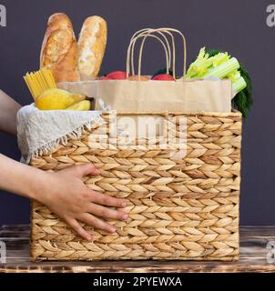 Verdure, verdure e frutta, cereali e pasta in un cestino di vimini nelle mani di un bambino. Consegna o donazione di cibo. Foto Stock