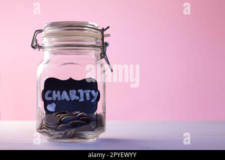 Vaso di vetro con monete con gesso tag Charity su sfondo rosa. Concetto di donazione e carità. Spazio di copia. Foto Stock