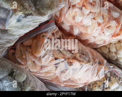 Ci sono molti grandi sacchetti di plastica con i gamberetti surgelati crudi e bolliti sul banco del mercato del pesce. Foto Stock