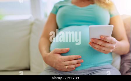 Inviare un conto alla rovescia per i suoi vicini. Primo piano di una donna incinta che SMS sul suo cellulare a casa. Foto Stock