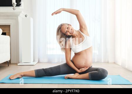 La gravidanza non è mai una scusa per non rimanere in forma. una donna incinta che fa yoga su un tappetino per l'esercizio fisico a casa. Foto Stock