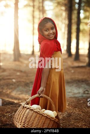 Im off per visitare la nonna. Ritratto di una bambina vestita con un mantello rosso e che tiene un cesto nel bosco. Foto Stock