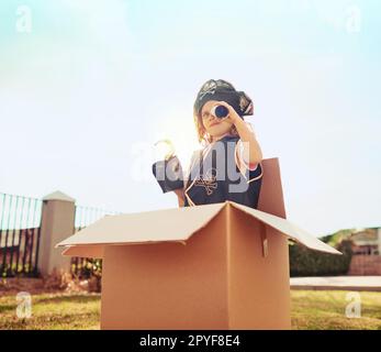 L'immaginazione è il suo giocattolo preferito. una bambina carina in un costume pirata che gioca in una scatola di cartone nel suo cortile. Foto Stock