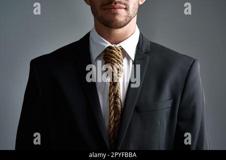 Siete diventati schiavi del commercio. Scatto in studio ritagliato di un uomo d'affari con un cappio legato intorno al collo per una cravatta su sfondo grigio. Foto Stock