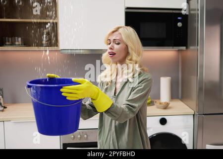 Donna preoccupata che tiene il secchio mentre le goccioline d'acqua perdono Foto Stock