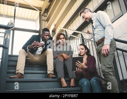 Nuovi spazi significano nuove idee. un gruppo eterogeneo di colleghi ha un incontro improvvisato con una tavoletta sulle scale. Foto Stock