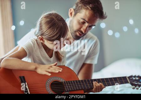 Creare una bella musica insieme. una bambina che suona la chitarra con suo padre. Foto Stock