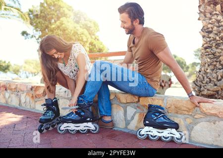 Ne avrai la possibilità. una donna che aiuta il suo ragazzo a mettere su rollerblade in un parco. Foto Stock