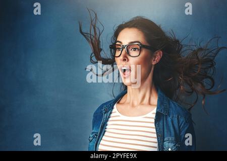 WOah che ha acceso l'aria condizionata. Studio shot di una giovane donna con aria soffiata in faccia su uno sfondo blu. Foto Stock