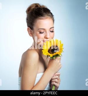 Bellezza che è naturalmente perfetta. Studio shot di una bella giovane donna che odora un girasole. Foto Stock