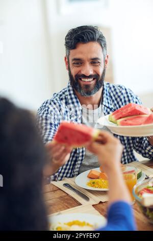 È la loro delizia estiva preferita. una famiglia felice si è riunita intorno al loro tavolo per un pasto. Foto Stock