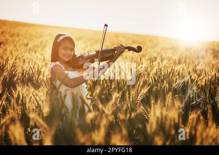 Natura piccolo maestro. Ritratto di una ragazza carina che suona il violino mentre si trova in un campo di grano. Foto Stock