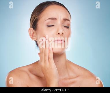 Mal di denti, igiene dentale e igiene orale con una donna modello che le tiene il viso in dolore su sfondo blu. Dentista, cavità e bocca con una giovane donna attraente che tocca la guancia in studio Foto Stock