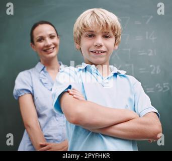 HES ispirato dal suo insegnamento. Un ragazzo che gli attraversa le braccia mentre il suo maestro si trova sullo sfondo della lavagna. Foto Stock