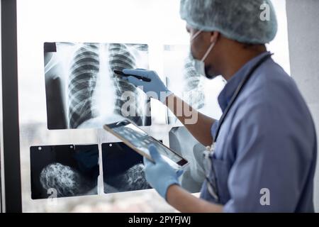 Focus sull'esame radiografico del torace studiato da un operatore sanitario multirazziale in indumenti protettivi utilizzando un tablet con penna stilo. Radiologo maschile i Foto Stock