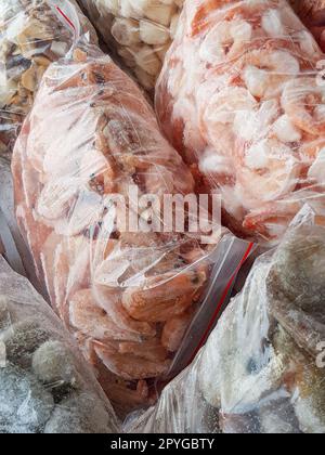 Ci sono molti grandi sacchetti di plastica con i gamberetti surgelati crudi e bolliti sul banco del mercato del pesce. Foto Stock