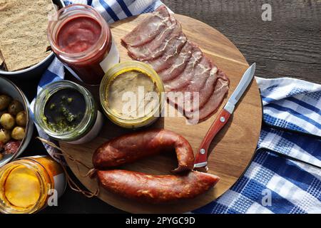 Tagliere con prosciutto, salame, bastoncini di pane, olive e snack su fondo di pietra scura. Vista dall'alto Foto Stock