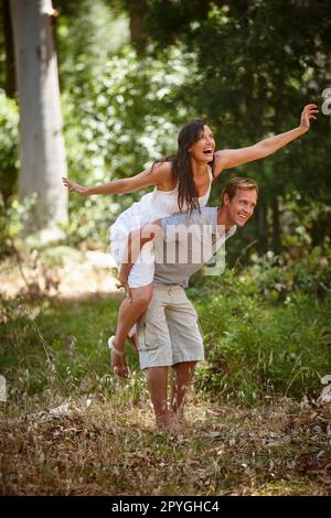 La foresta è il loro luogo felice. un uomo piggybacking la sua ragazza nella foresta. Foto Stock