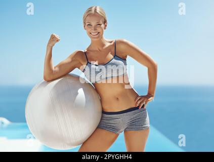 Im con base in abs. una giovane donna attraente flexing il suo bicep su una sfera di esercitazione dalla piscina dopo il suo workout. Foto Stock