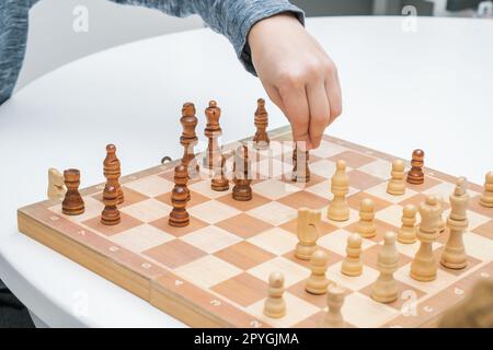 Irriconoscibile tenete la mano e muovete il pedone degli scacchi, giocate a scacchi su una tavola di legno su un tavolo bianco. Sport da tavolo Foto Stock