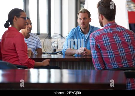 Portare le loro idee al tavolo. Quattro colleghi seduti attorno a un tavolo e discutendo alcune idee. Foto Stock