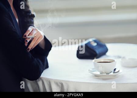 Accessori classici di ricchezza e stile. una donna elegante seduta a un  tavolo che fuma con una tazza di caffè davanti a lei Foto stock - Alamy