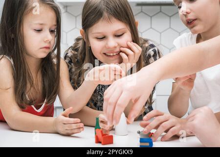 Bambini sorridenti e concentrati che giocano con i giocattoli dei mobili su un tavolo bianco. Immaginazione e giochi creativi per bambini Foto Stock