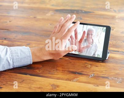 Raggiungere .... vista ritagliata di una mano di un giovane mans che sventolano verso la sua famiglia in una videochiamata. Foto Stock