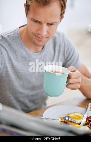 Gli piace sapere cosa succede nel mondo. un bell'uomo che legge il giornale mentre fa colazione. Foto Stock