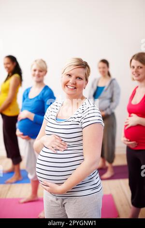 Ottenere il massimo dalla maternità. Un gruppo multietnico di donne incinte in piedi in una classe di esercizio sorridendo felicemente alla macchina fotografica. Foto Stock