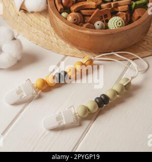 Clothespin in plastica bianca con perline di legno bianco, nero e arancione su lacci bianchi per succhietti vicino al recipiente in legno. Foto Stock