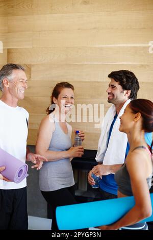 Chiacchierare in palestra. Giovane coppia e coppia matura in abbigliamento sportivo che parlano tra loro. Foto Stock