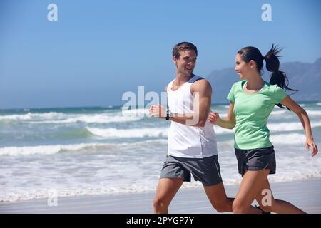 Questo è un tipo di amore sportivo. una giovane coppia che fa jogging insieme sulla spiaggia. Foto Stock