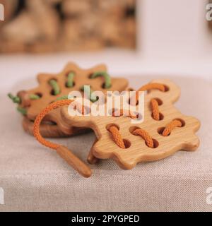 Giocattoli in legno per bambini con fori per l'allacciatura con cordoncino arancione e verde sulla panca beige contro il caminetto. Telaio quadrato Foto Stock