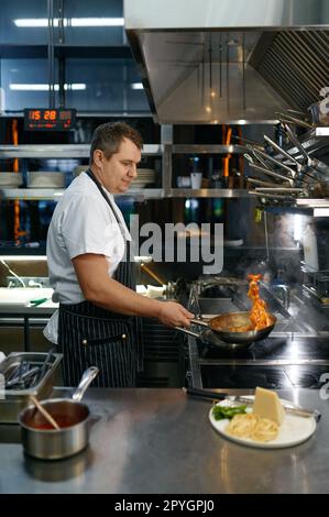 Chef che lancia pasta calda all'aria in padella, processo di cottura Foto Stock