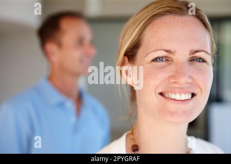 Cant immaginare la mia vita senza di lui. una bella donna sorridente alla macchina fotografica con suo marito sullo sfondo. Foto Stock