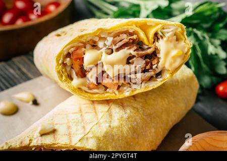 Shawarma al formaggio con salsa al formaggio, pollo e verdure in pita pane su superficie di legno, pomodori ciliegini e prezzemolo Foto Stock