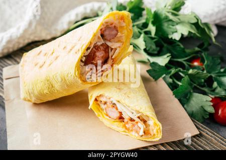 Arrotolare con salsicce e verdure. Hot dog con pita su carta artigianale con pomodori ciliegini e prezzemolo verde Foto Stock