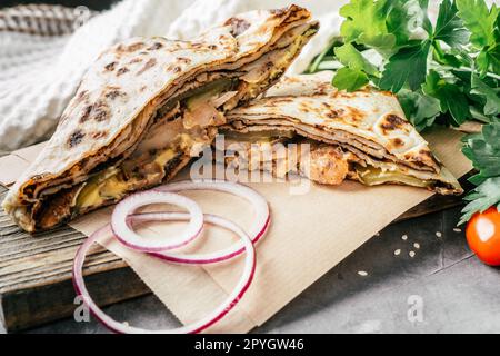 Pancake sottile a fette con pollo, cetriolo sottaceto, salsa al formaggio, cipolla su superficie di legno scuro, con prezzemolo verde Foto Stock