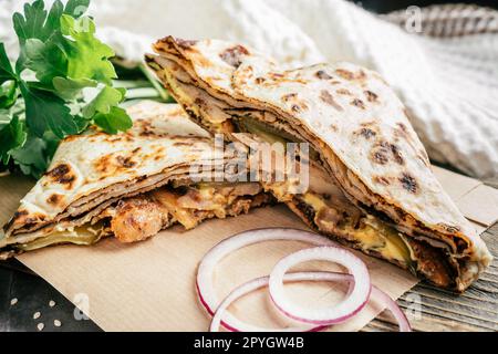 Pancake sottile a fette con pollo, cetriolo sottaceto, salsa al formaggio, cipolla su superficie di legno scuro, con prezzemolo verde Foto Stock