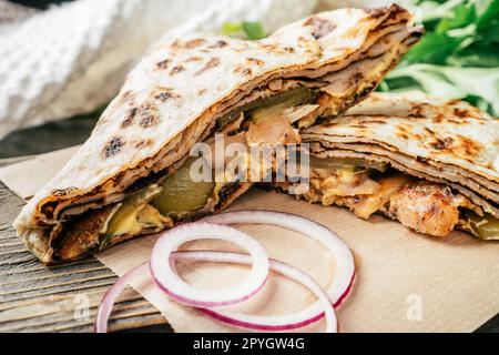 Pancake sottile a fette con pollo, cetriolo sottaceto, salsa al formaggio, cipolla su superficie di legno scuro, con prezzemolo verde Foto Stock