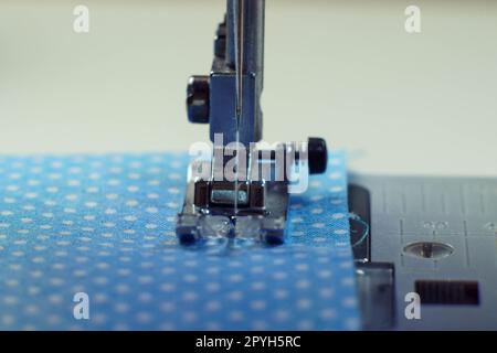 Primo piano dettagliato del piede in acciaio della macchina da cucire con ago e cuciture del filo su tessuto a pois in tessuto blu Foto Stock