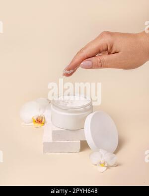 Una donna che usa la crema del vaso aperto con un coperchio vuoto vicino a fiori di orchidee, mockup Foto Stock