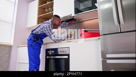 Il giovane riparatore ripara il filtro estrattore per cucine Foto Stock