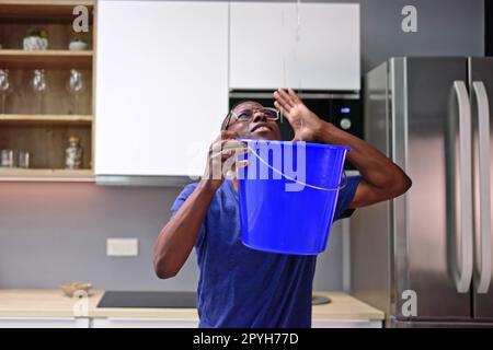 Uomo preoccupato che tiene il secchio mentre perde acqua dal soffitto Foto Stock