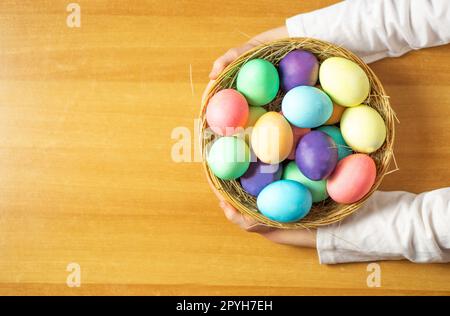 Una ragazza, di cinque anni, che tiene in mano un cesto di legno con molte uova di Pasqua colorate. Foto Stock